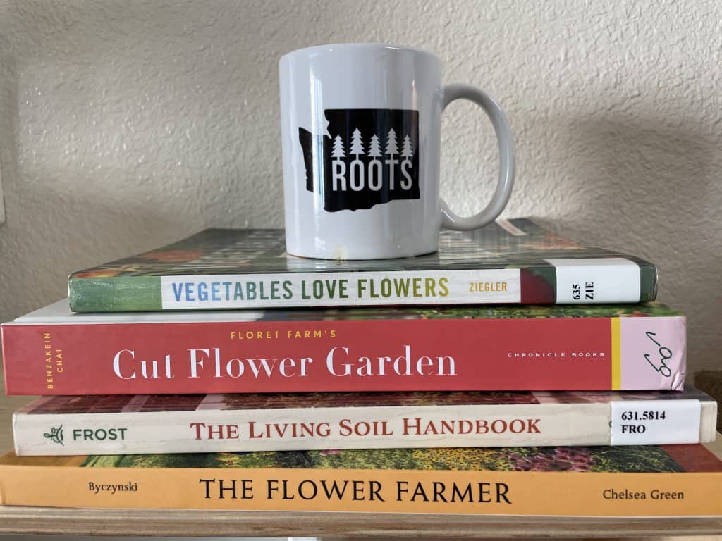 A stack of gardening books with a coffee mug sitting on top. 